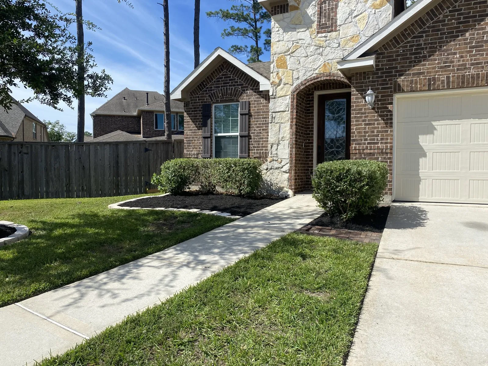 Neatly trimmed shrubs beside a front entry path and mulched planting beds