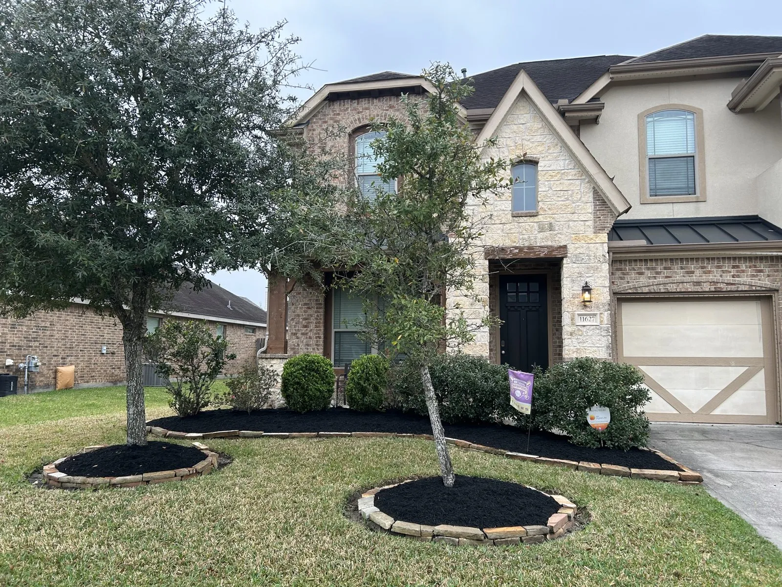 Fresh dark mulch and shrubs across the front of a brick-and-stone home