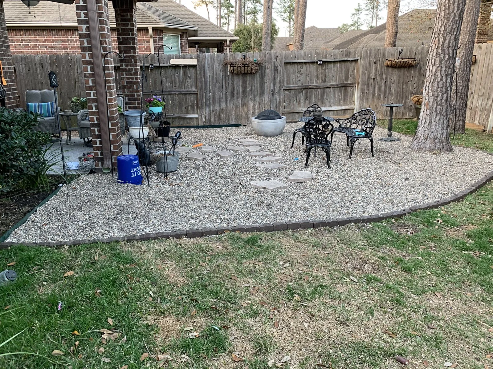 A gravel seating area with chairs, stepping stones and a fire bowl beneath mature trees