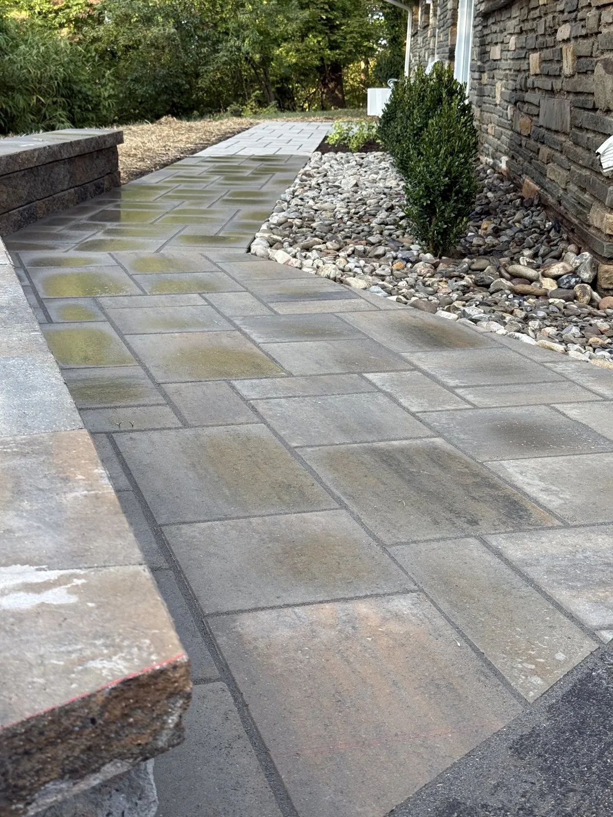 Paved walkway beside a river-rock planting bed and a low block wall